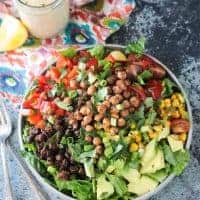 Big plate of salad with avocado, black beans, red peppers,tomatoes, corn, and crunchy roasted chickpeas.