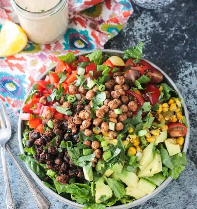 Big plate of salad with avocado, black beans, red peppers,tomatoes, corn, and crunchy roasted chickpeas.