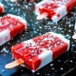 Red and white striped strawberry rhubarb coconut milk popsicles on a black background.