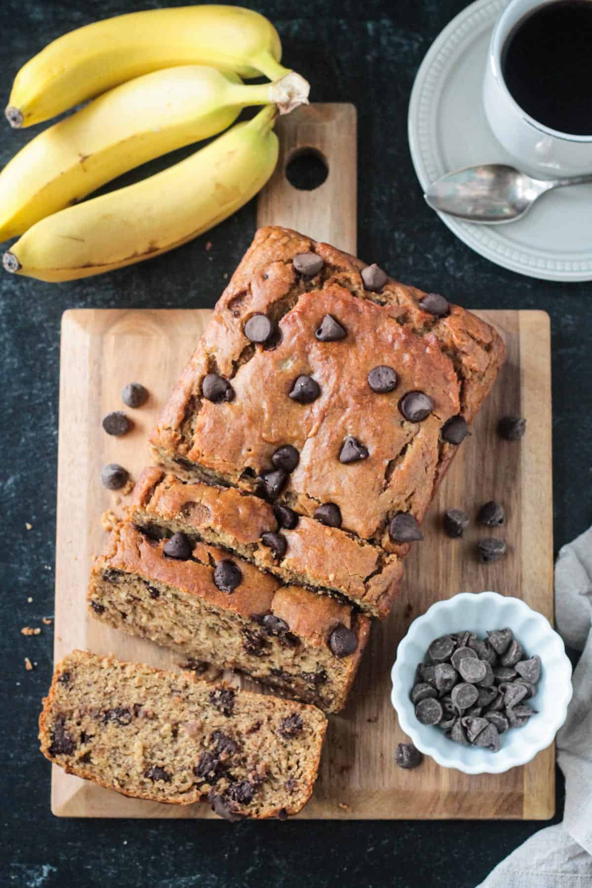 Sliced loaf of vegan peanut butter banana bread on a serving board next to a bunch of bananas.