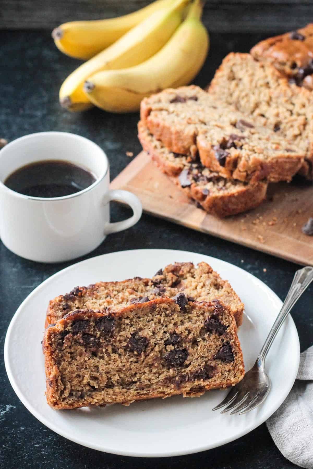 Two slices of peanut butter banana bread on a plate in front of the rest of the loaf on a tray.