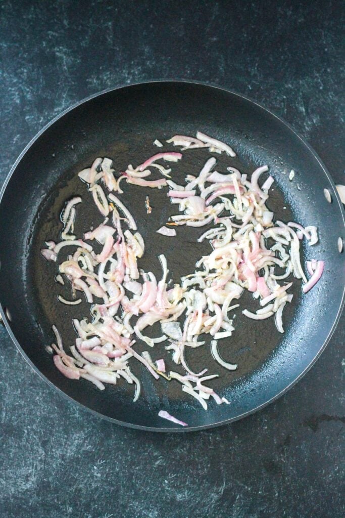 Sautéed sliced red onions in a skillet.
