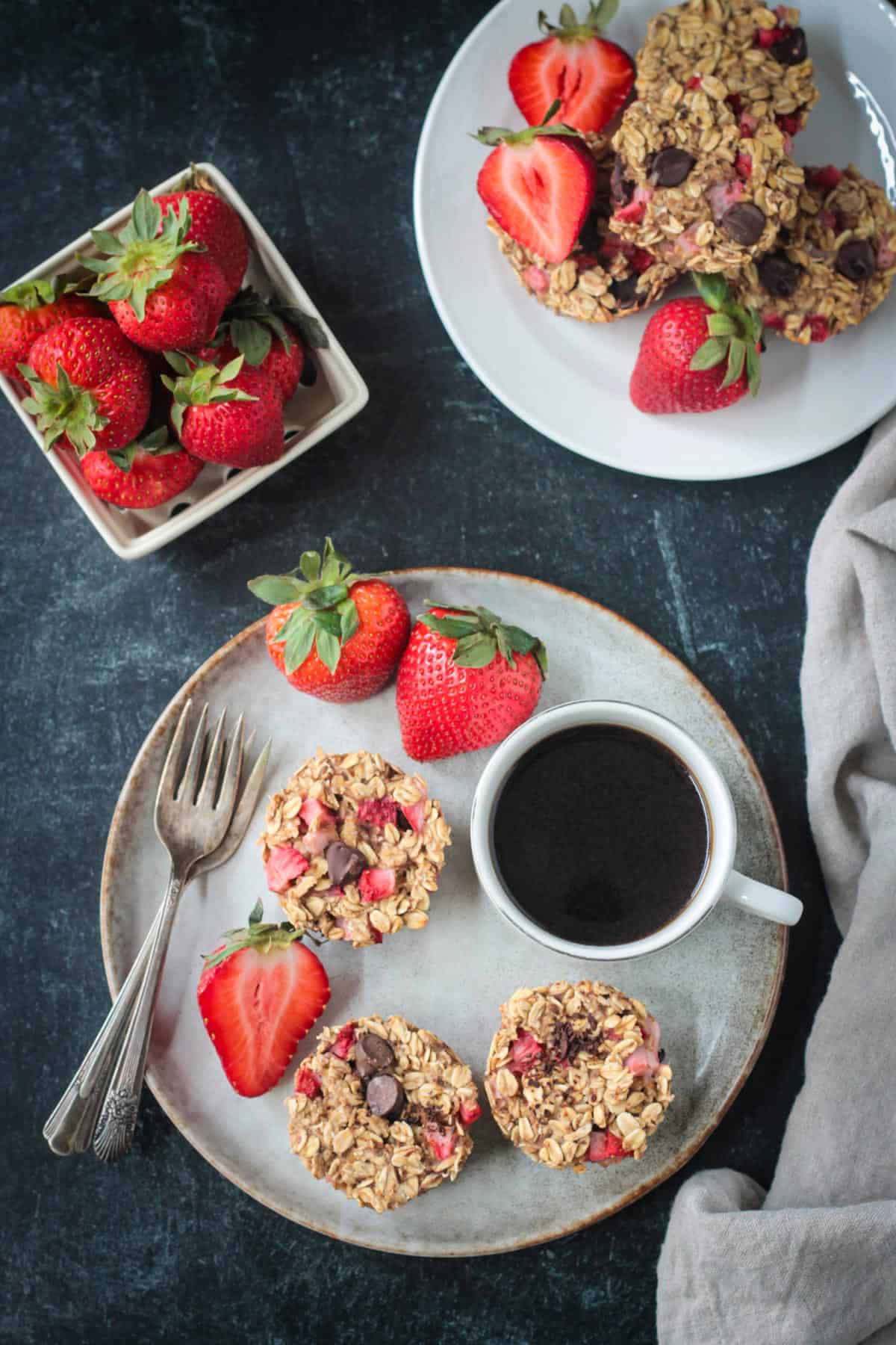 Banana Baked Oatmeal Bites with chunks of fresh strawberries and chocolate chips. Easily made in a muffin pan. A hearty, healthy breakfast or snack made with no refined sugars! Three strawberry baked oatmeal muffins on a plate with a cup of coffee and fresh strawberries.