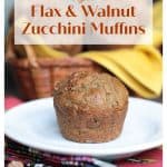 One muffin on a white plate in front of a basket of vegan zucchini muffins.