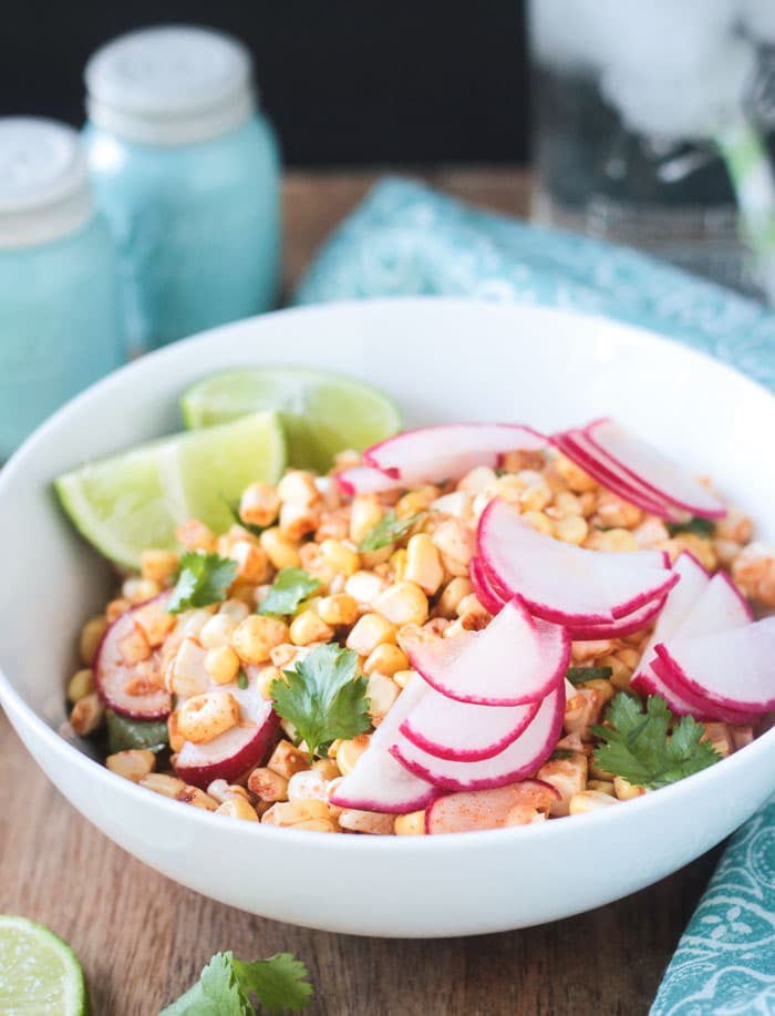 Thinly sliced radish slices on top of a corn radish salad with lime wedges.