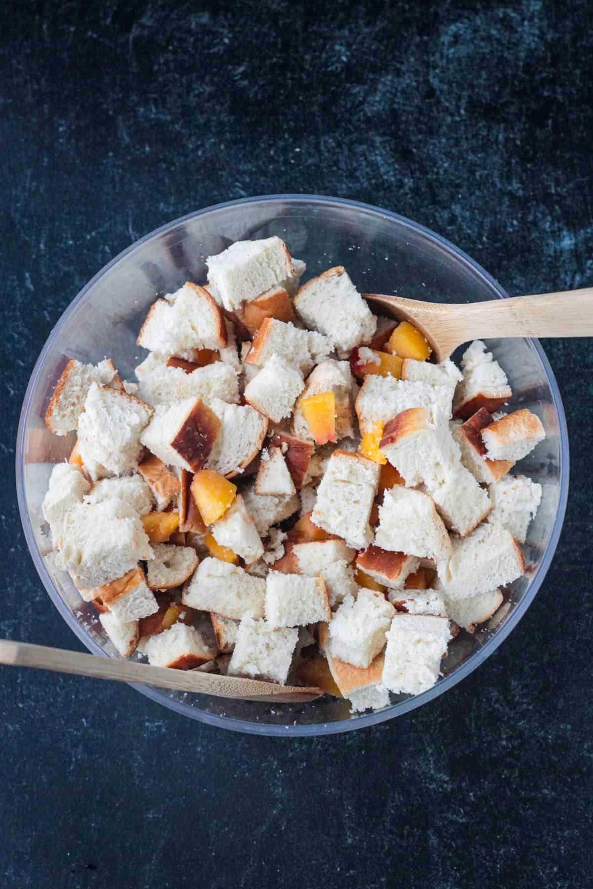 Cubed bread and diced peaches mixed in a large bowl.