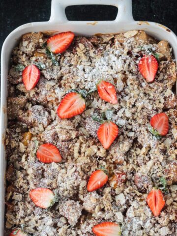 Baked casserole garnished with halved fresh strawberries and a sprinkle of powdered sugar.