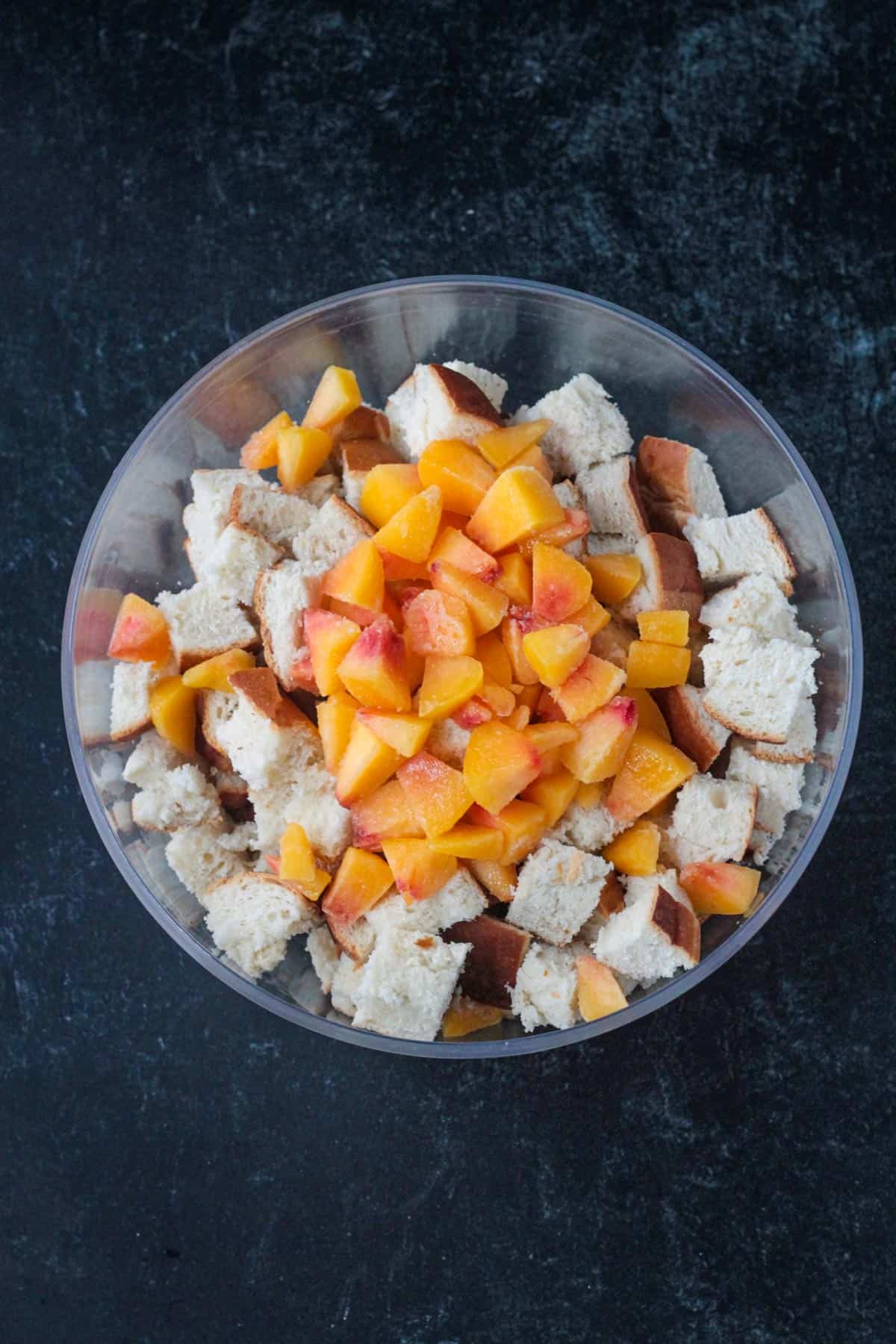 Diced peaches in a bowl on top of cubed bread.