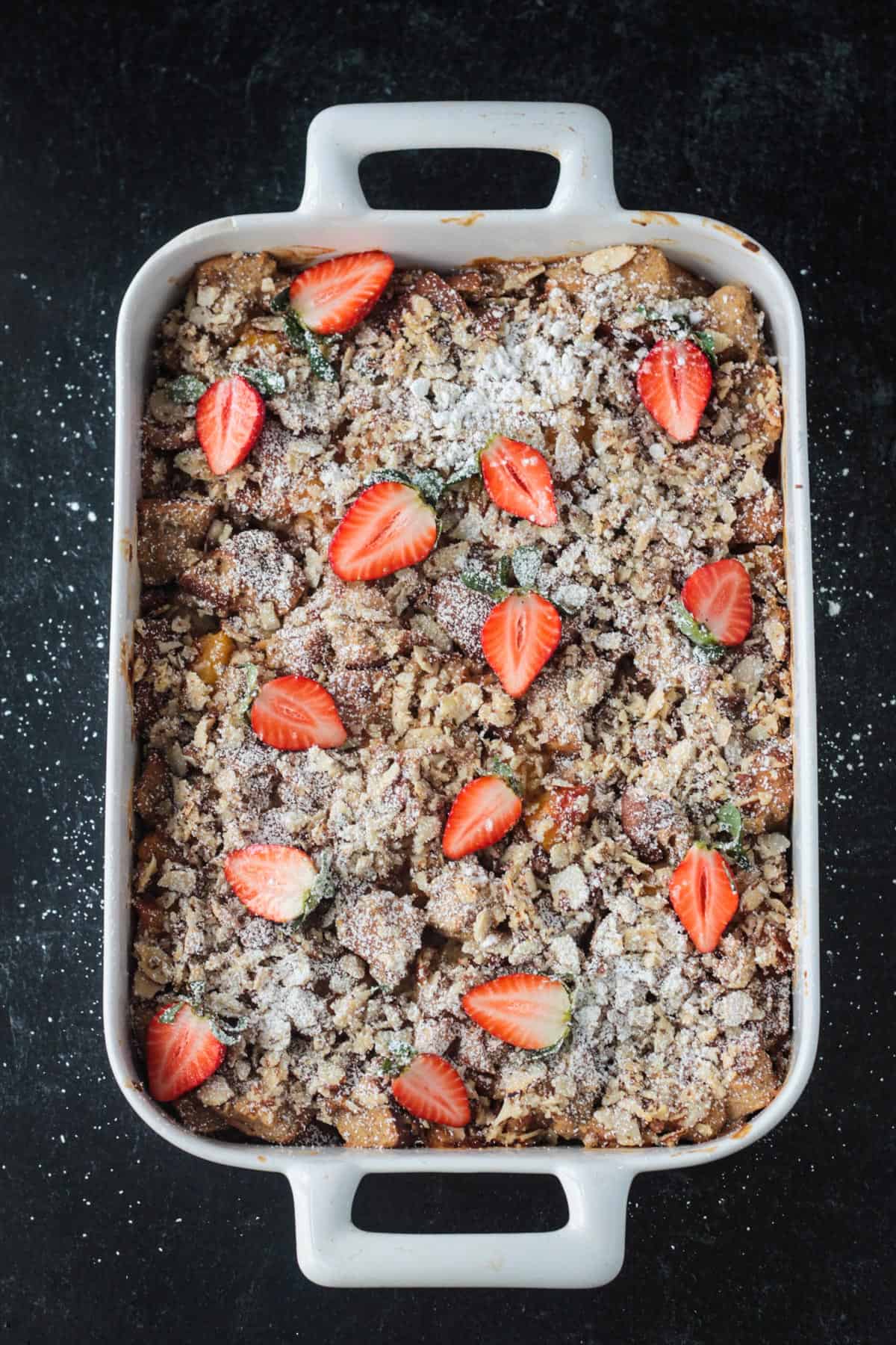 Baked casserole garnished with halved fresh strawberries and a sprinkle of powdered sugar.