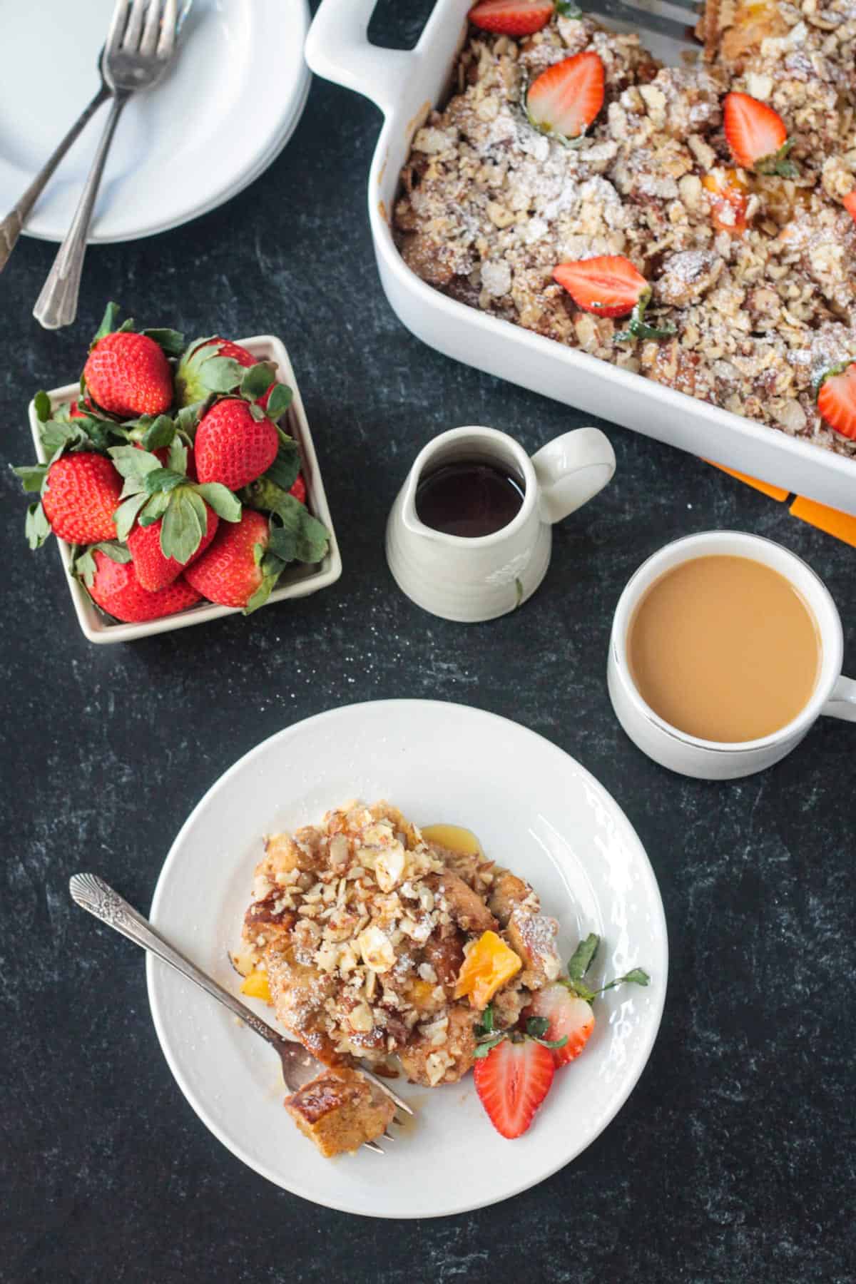 Vegan french toast casserole on a plate next to the serving dish, cup of coffee, and fresh strawberries.