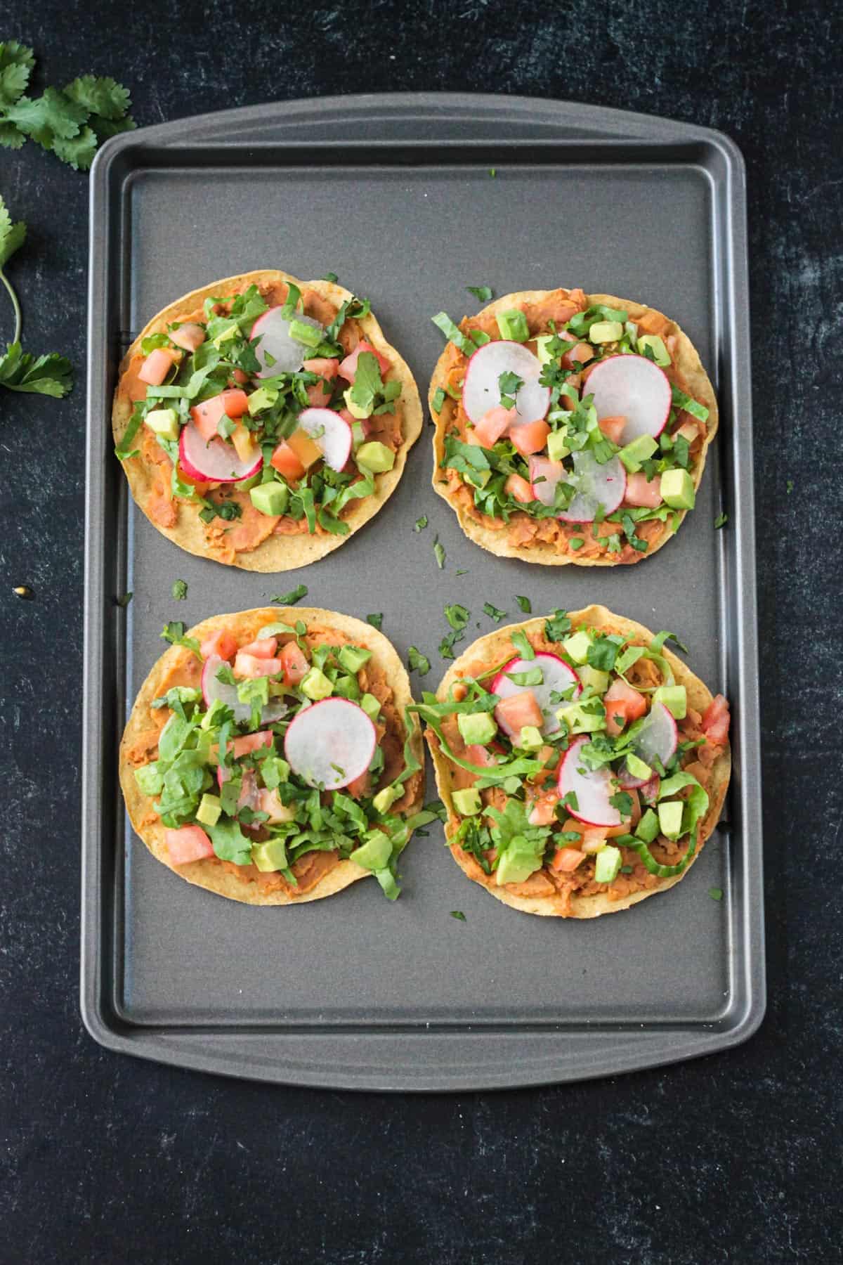 4 crispy corn tortillas topped with beans, lettuce, and tomato, avocado, and cilantro.