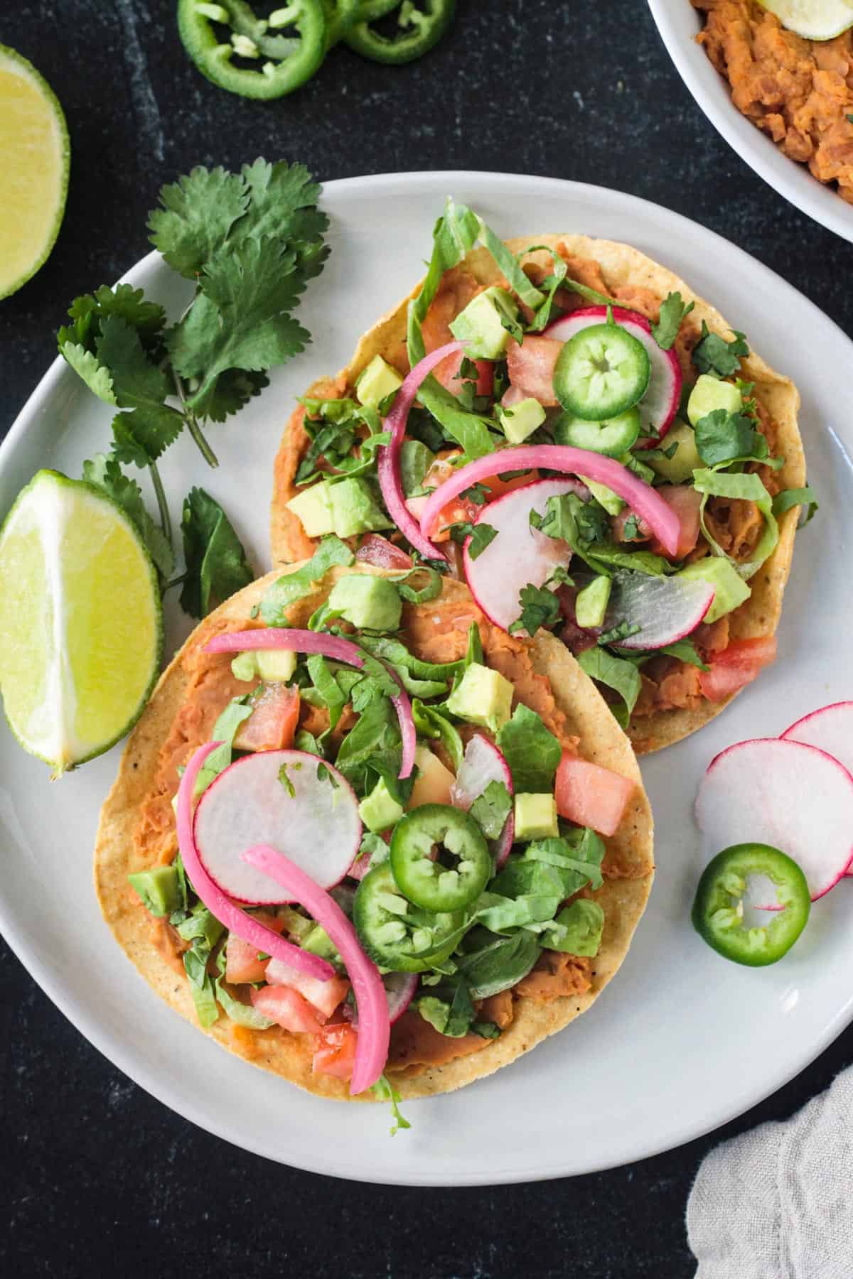 Two crispy baked flat tortillas with lots of toppings next to a lime wedge.