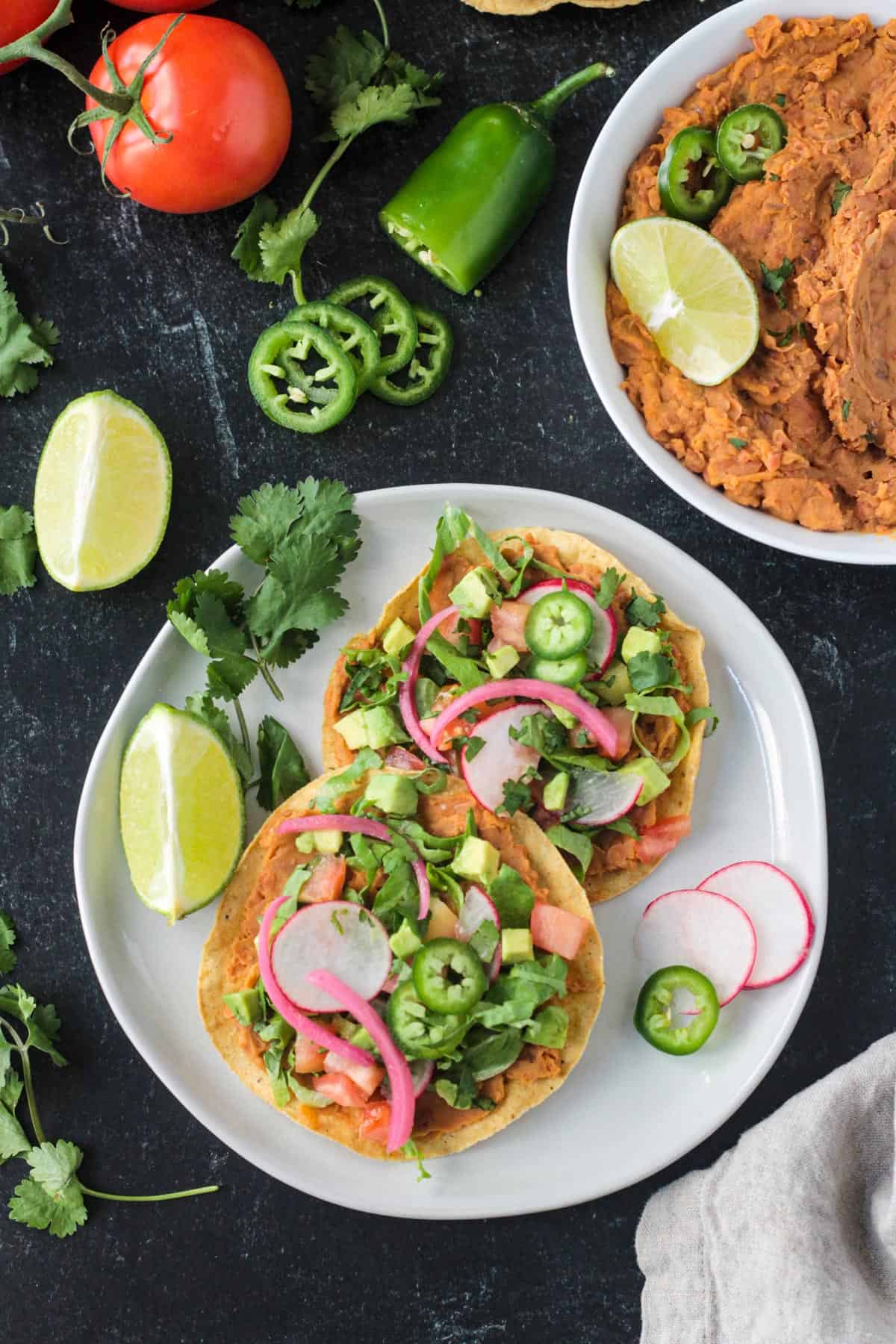 Vegan tostadas with refried beans and lots of toppings on a plate.