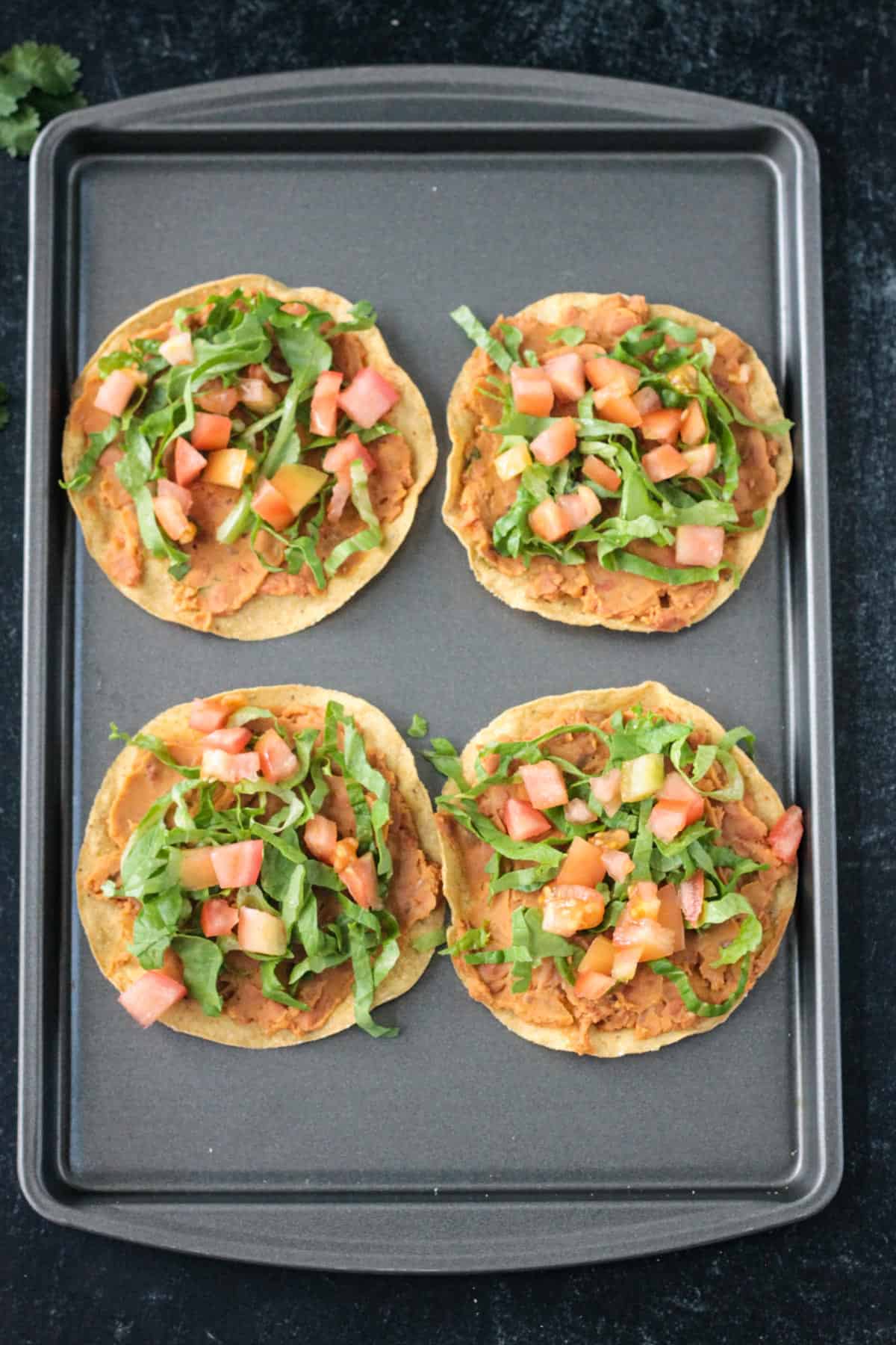 4 crispy corn tortillas topped with beans, lettuce, and tomato.