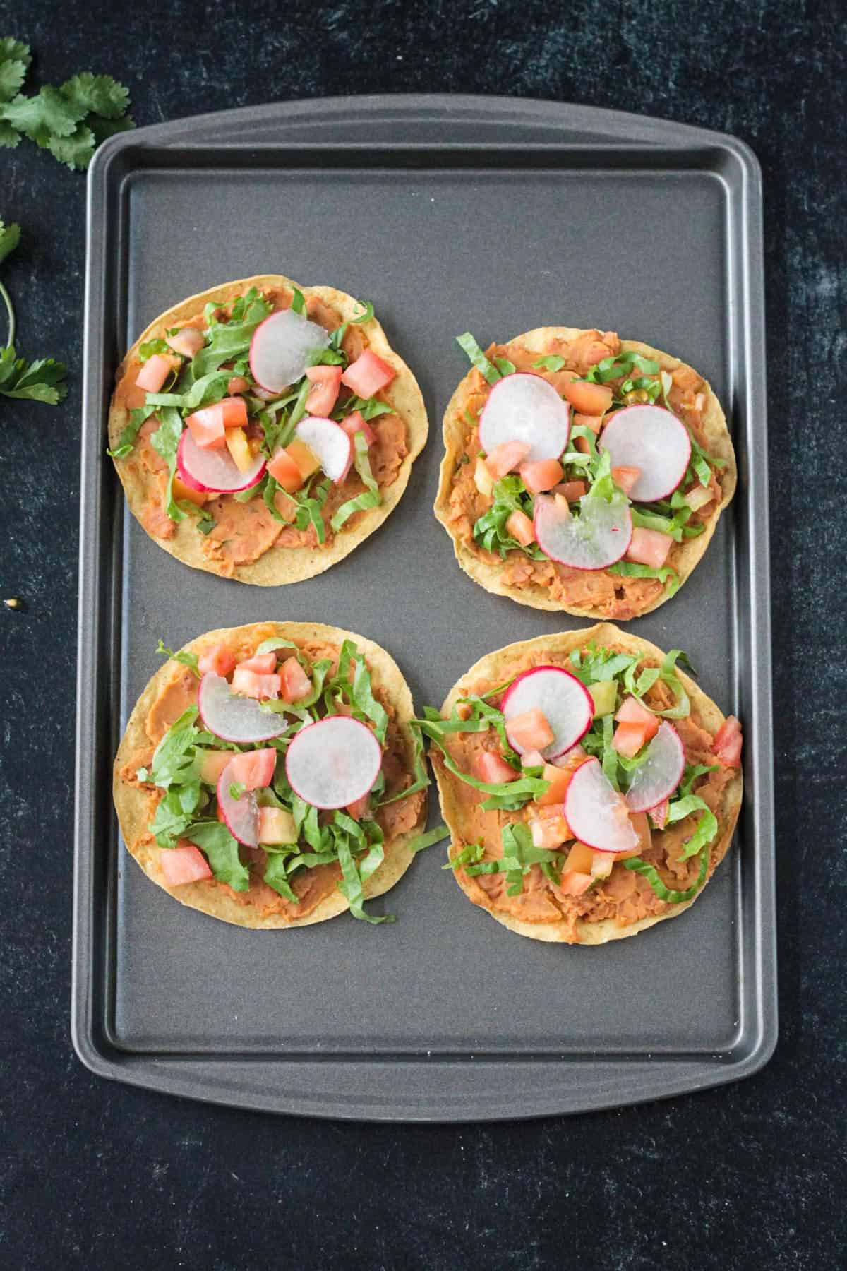 4 crispy corn tortillas topped with beans, lettuce, tomato, avocado, and radishes.