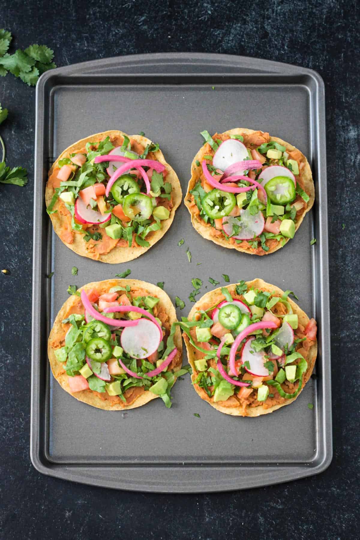 4 crispy corn tortillas topped with beans, lettuce, tomato, avocado, radishes, and onion.