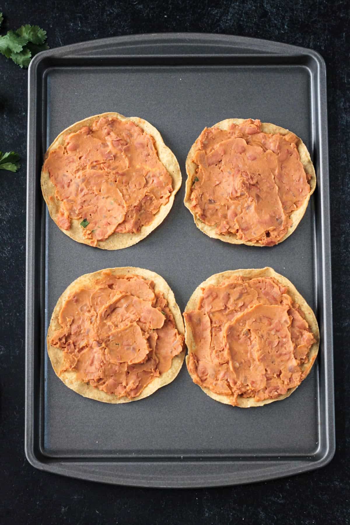 Refried beans spread on 4 tostada shells.