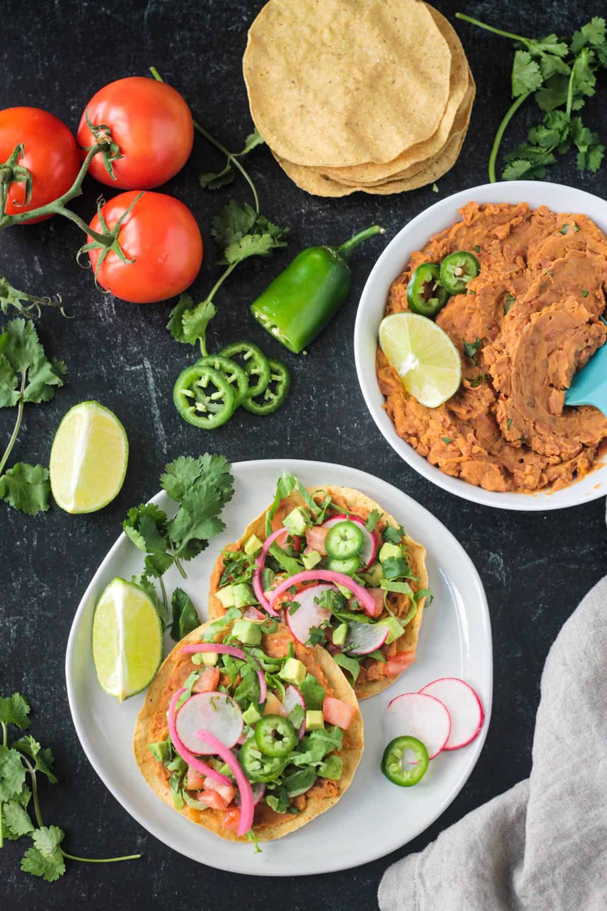 Two vegan tostadas on a plate next to a bowl of refried benas.