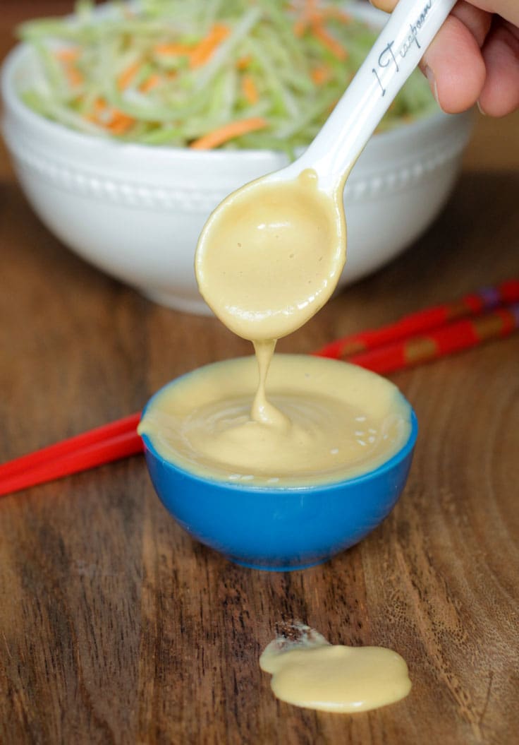 Creamy sesame salad dressing being drizzled from a spoon into a small bowl.