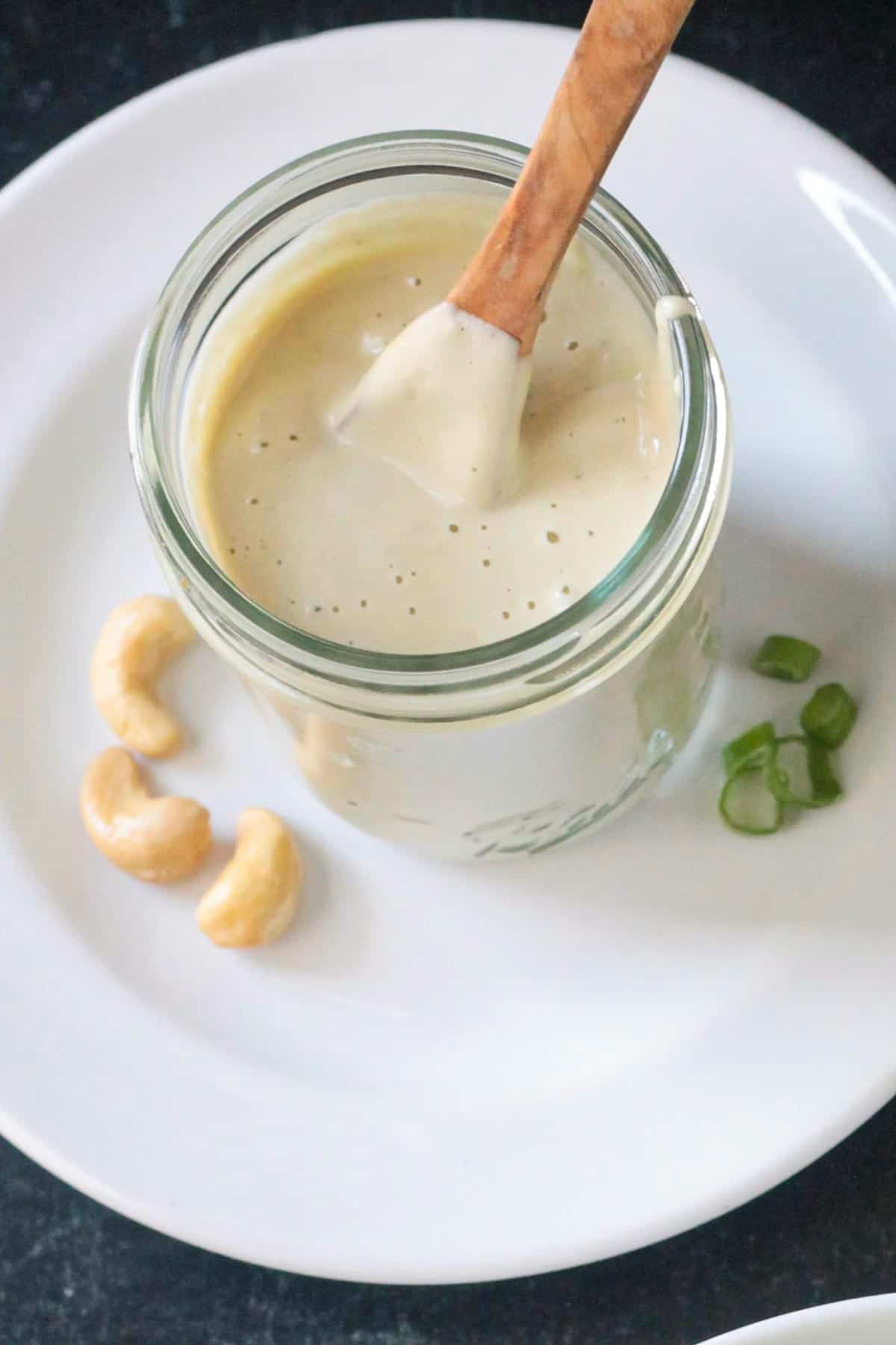 Small wooden spoon in a jar of creamy sesame salad dressing.