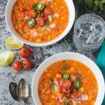 Two bowls of summer corn chowder topped with halved cherry tomatoes, jalapeno slices, and green onions.