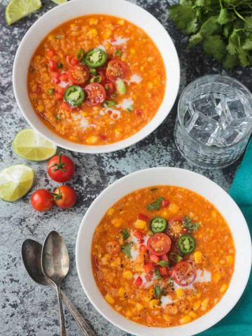 Two bowls of summer corn chowder topped with halved cherry tomatoes, jalapeno slices, and green onions.