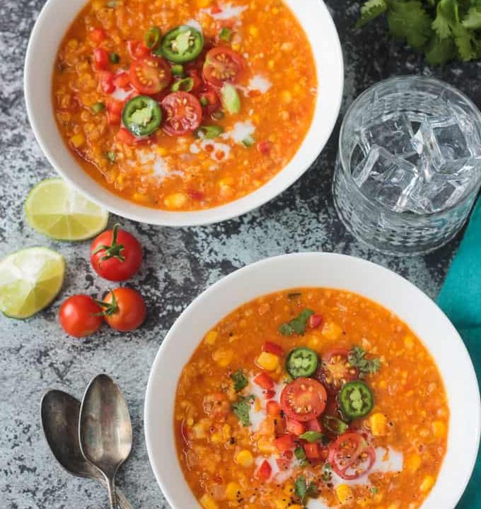 Two bowls of summer corn chowder topped with halved cherry tomatoes, jalapeno slices, and green onions.