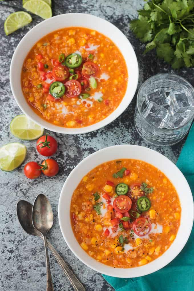 Two bowls of summer corn chowder topped with halved cherry tomatoes, jalapeno slices, and green onions.