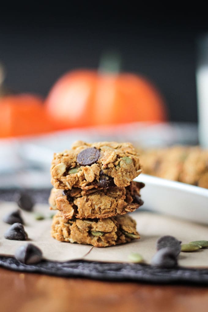 Stack of Crunchy Gluten Free Pumpkin Oatmeal Chocolate Chip Cookies. Decorative orange pumpkins in the background.