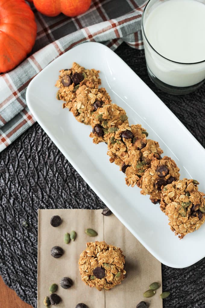 Crunchy Pumpkin Oatmeal Chocolate Chip Cookies lined up on a rectangular white platter. Glass of milk next to the platter.