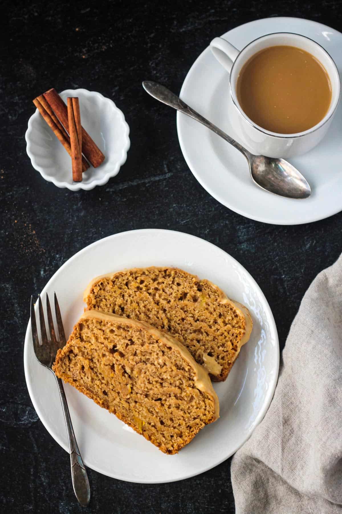 Two slices of butternut squash bread on a plate next to a cup of coffee.