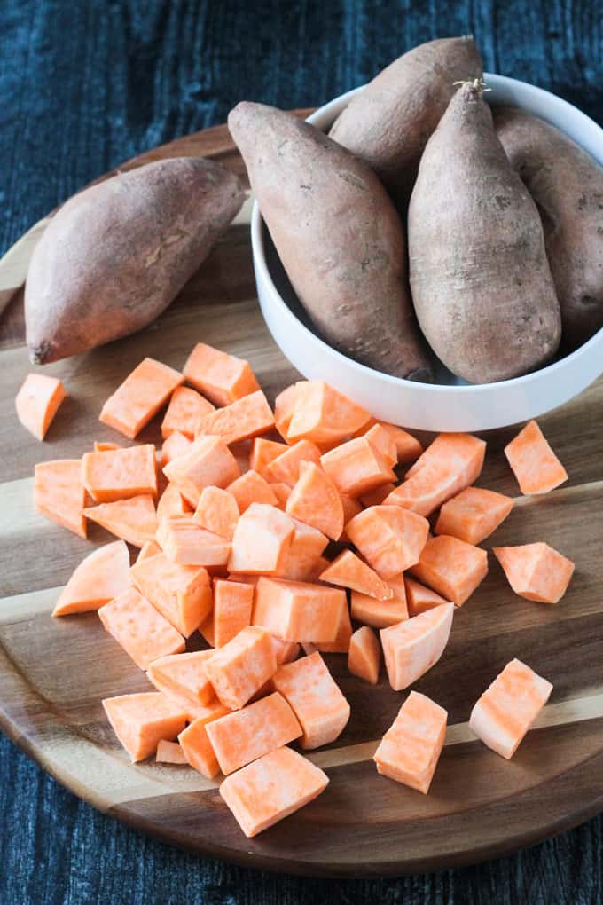 Diced sweet potato in front of a bowl of whole sweet potatoes