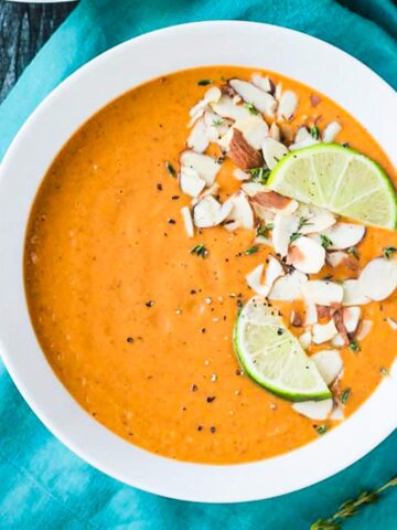 Bowl of vegan sweet potato soup topped with shaved almonds and lime wedges.