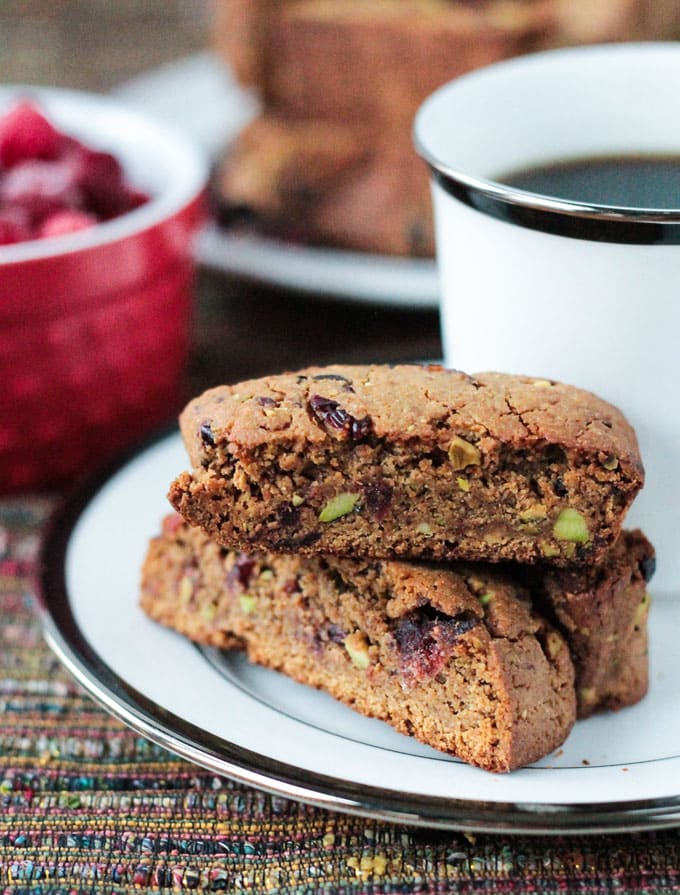 Stack of three Whole Wheat Cranberry Pistachio Vegan Biscotti on a plate with a cup of coffee.