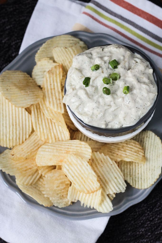 Plate of potato chips surrounding a bowl of french onion dip garnished with green onions.