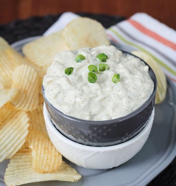 Vegan French Onion Dip in a bowl surrounded by ridged potato chips.