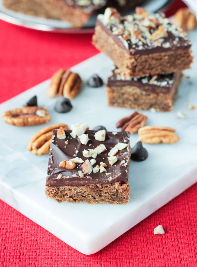 One vegan toffee bar on a white tray in front of a stack of two more dessert bars.