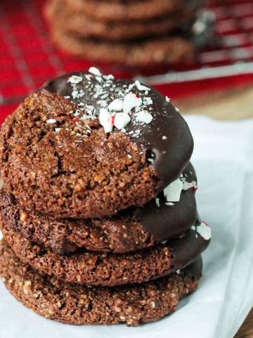 Stack of 4 chocolate molasses cookies partially dipped in chocolate and sprinkled with crushed peppermint candies.