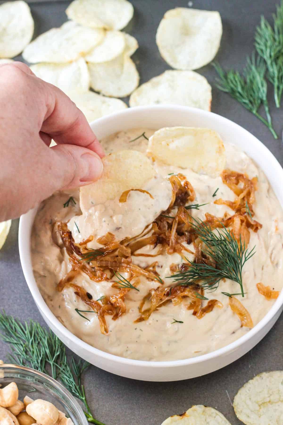 Adult hand dipping a potato chip into a bowl of french onion dip.