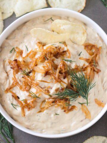 Vegan French Onion Dip in a serving bowl topped with extra caramelized onions and fresh dill.