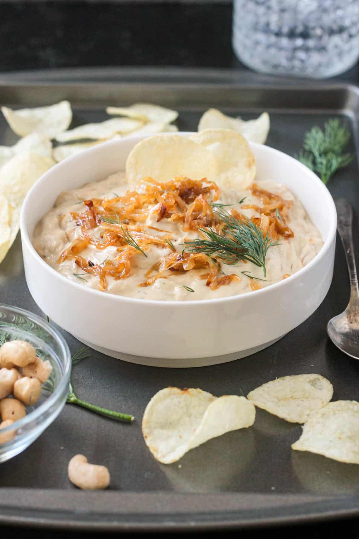 Bowl of caramelized onion dip on a tray with potato chips.