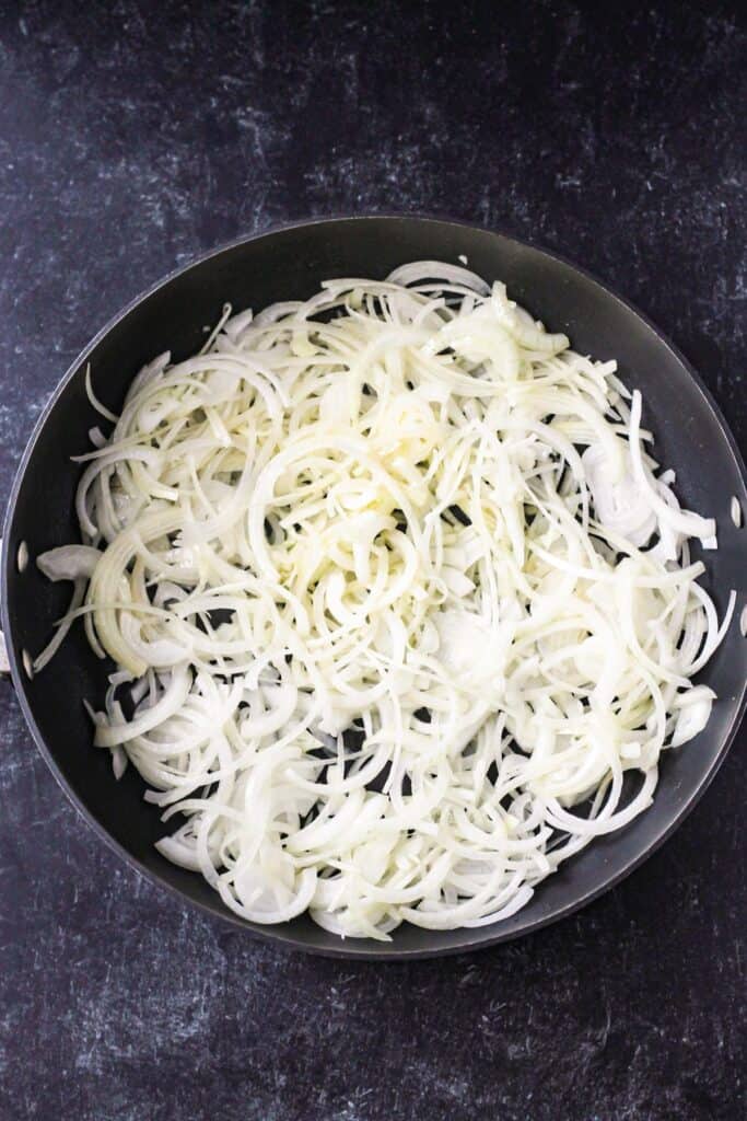 Raw onions in a skillet with oil.