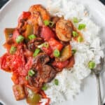 Close up of saucy sliced mushrooms, tomatoes, and peppers plated over white rice.