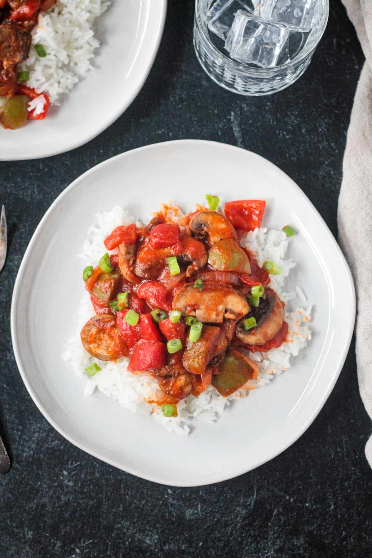 Vegan Pepper Steak with mushrooms and onions served over rice and garnished with sliced green onions.