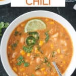 Vegan white bean chili in a bowl with a spoon and garnished with chopped cilantro leaves and a lime wedge.