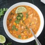 Vegan white bean chili in a bowl with a spoon and garnished with chopped cilantro leaves and a lime wedge.