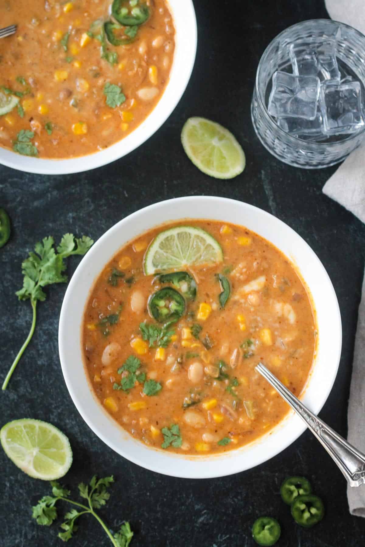 Vegan white bean chili in a bowl with a spoon and garnished with chopped cilantro leaves and a lime wedge.