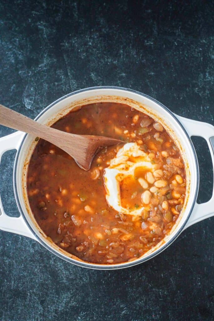 Adding vegan sour cream to the pot of chili.