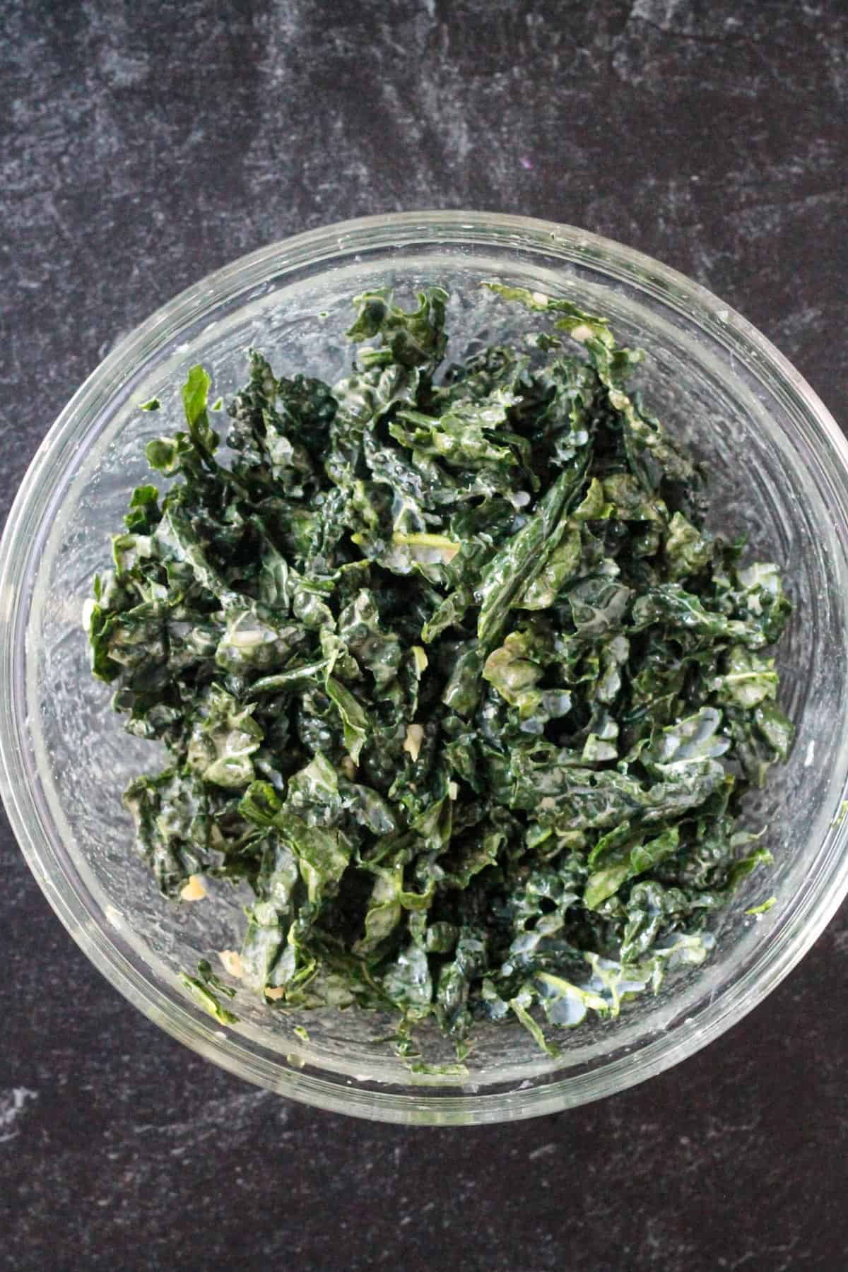 Chopped kale mixed with the mustard dressing in a glass mixing bowl.