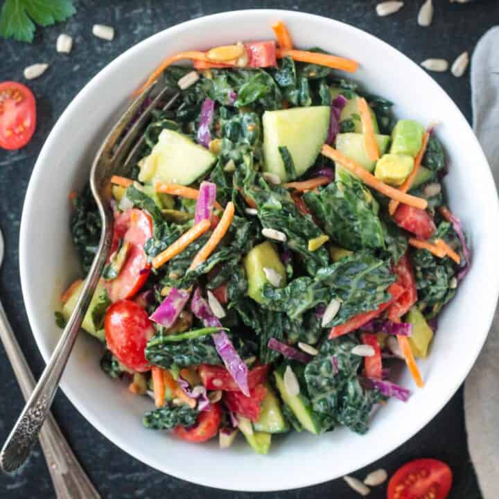 Chopped kale salad with a variety of vegetables in a white bowl.